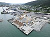Utsikt over et stort anleggsområde ved sjøen med kraner, betongkai og steinfylling.