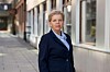 En kvinne i mørk jakke står på et fortau foran en bygning.