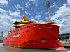 Stort rødt spesialskip fortøyd i en havn under en skyet blå himmel.